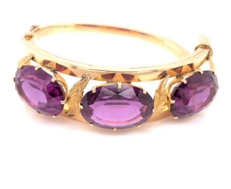 AN ANTIQUE 14ct YELLOW GOLD THREE STONE HINGED BANGLE. THE THREE PRINCIPLE OVAL CUT FACET SYNTHETIC COLOUR CHANGE CORUNDUM ST