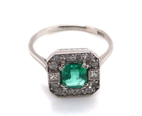 A VINTAGE ART DECO STYLE EMERALD AND DIAMOND HALO SET RING. THE CENTRAL EMERALD A MIXED CUT SURROUNDED BY A FRAME OF GRAIN SE