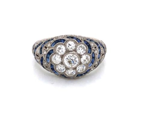 A SAPPHIRE AND DIAMOND BOMBAY RING. A CENTRAL DAISY CLUSTER WITH RADIATING SAPPHIRE AND DIAMOND ARCHES. UNHALLMARKED AND ASSE