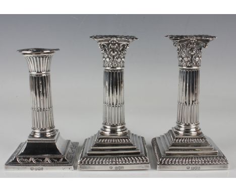 A pair of Edwardian silver Corinthian column candlesticks, each with a detachable nozzle, on a square stepped and gadrooned b
