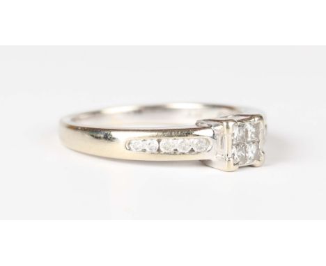 A white gold and diamond ring, mounted with four princess cut diamonds between circular cut diamond channel set sides, detail