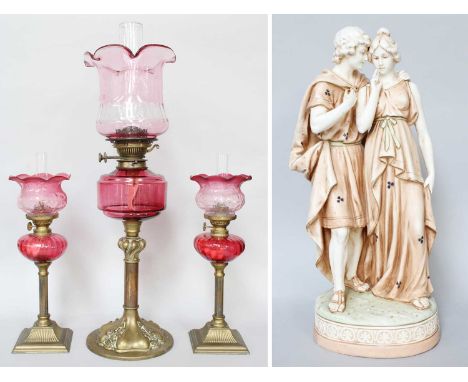A Pair of Victorian Brass Based Oil Lamps with cranberry glass resovoirs and shades; together with a larger example and a con
