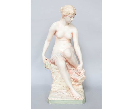 A Czechoslovakian Earthenware Figure of a Female Bather, the nude woman seated on a rocky outcrop, drying her foot, stamped 9