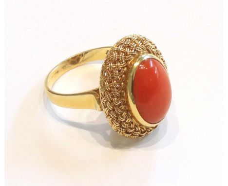An 18 Carat Gold Coral Ring, the oval cabochon coral within a yellow basket weave design setting, to a tapered shoulder plain