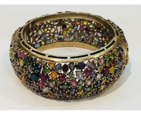 A 9ct yellow gold wide hinged bangle, encrusted with a variety of multi coloured gemstones including topaz, amethyst, garnet 