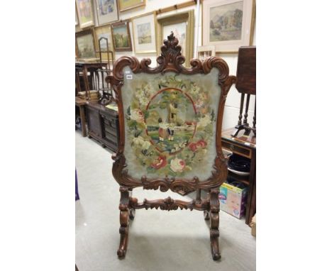 Large mahogany firescreen with ornate scroll carved frame inset with a glazed silk embroidery depicting three children playin