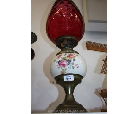 A brass Oil Lamp with china floral reservoir and cranberry tulip shaped shade (small chip to base), 21 1/2'' tall.
