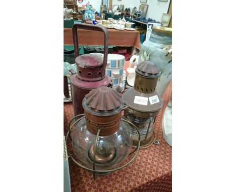 A red tin storm lamp together with a brass starboard lamp and a copper hanging lamp.