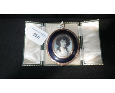 A 19th century painted miniature portrait of a lady wearing a white and blue dress in a yellow metal and blue enamel frame wi