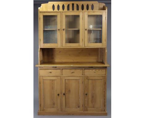 A pine dresser, the upper part with pierced stage back &amp; sides, fitted centre shelf enclosed by three glazed doors above 