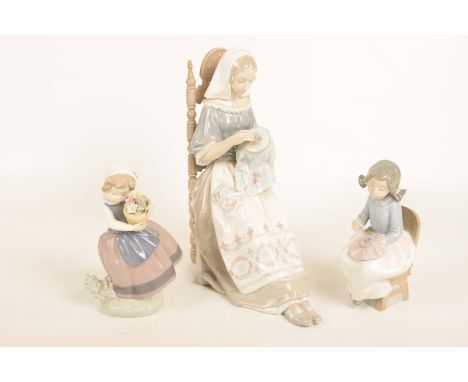 A Lladro figure of a young woman sewing, model sat in a ladder back chair along with a Lladro figure of a young girl holding 