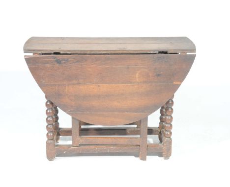 An 18th Century oval oak drop leaf dining tableHaving an oval plank top above a single frieze drawer raised on bobbin turned 