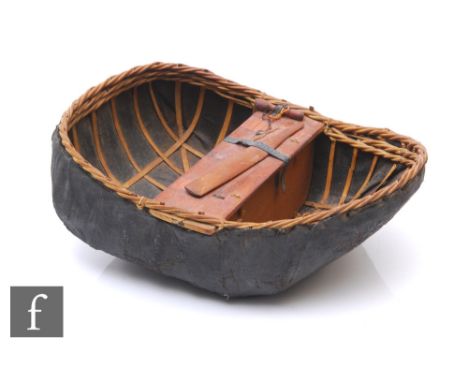 An early 20th Century wicker and leather covered model of a coracle with fixed wooden seat and paddle, width 26cm and a small