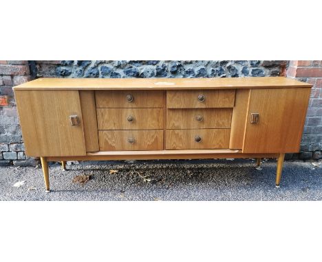 A 1970s design light teak sideboard, with six drawers to the centre flanked by a cupboard door either side, 77 cm high x 186 