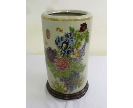 An Oriental cylindrical ceramic umbrella stand decorated with flowers and leaves on a carved wooden stand