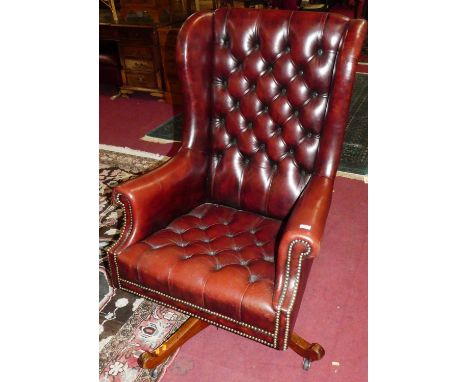 A burgundy buttoned leather upholstered and studded winged scroll swivel desk chair, raised on mahogany four-spoke base, w.76