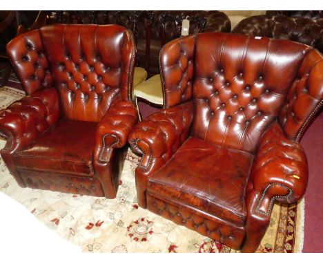 A pair of contemporary ox-blood buttoned leather upholstered winged scroll armchairs, each with studded detail and raised on 