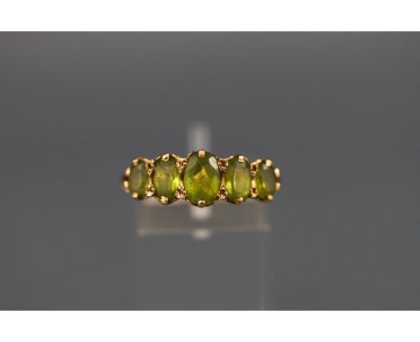 A hallmarked 9ct gold half hoop ring set with five graduated oval peridot. Scroll carved shoulders. Gross weight: 3.6 grams. 