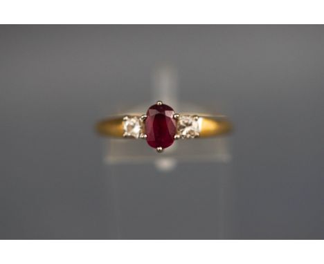 A hallmarked 18ct gold three stone ring set with an oval ruby measuring 6.5mm x 4.5m. Further set with two round brilliant cu