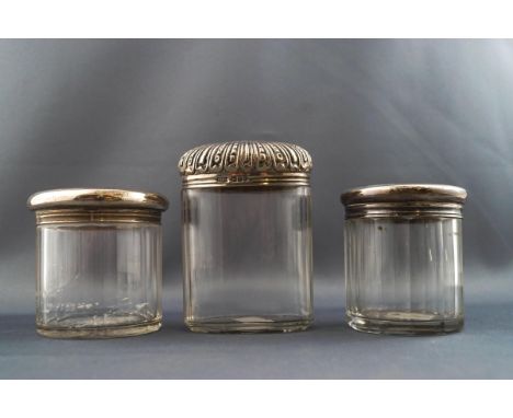 A cut glass oval dressing table jar with embossed silver cover, 9.5cm high, London 1902, together with two other cylindrical 