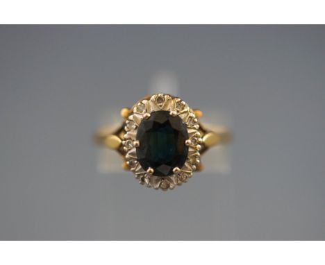 A hallmarked 18ct gold cluster ring set with an oval sapphire measuring 9.10mm x 7.00mm. Further set with twelve single cut d