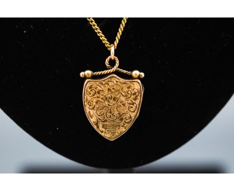 A hallmarked 9ct gold locket in the design of a shield having filigree scroll engraved design. suspended from a goldplated cu