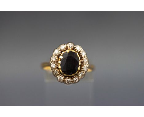 A yellow metal cluster ring set with an oval sapphire measuring 9.00mm x 6.50mm. Further set with fourteen round brilliant cu