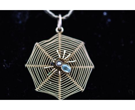 A yellow metal spider web pendant having a central spider set with aquamarine and seed pearl. Suspended from a flat link chai