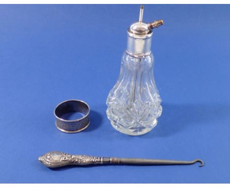 A silver button hook with floral and ribbon decoration, a silver collared cut glass atomiser and a silver napkin ring 