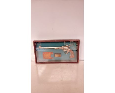 Framed Western-themed display featuring a replica long-barrel revolver, aged parchment, and decorative ammunition. Encased in
