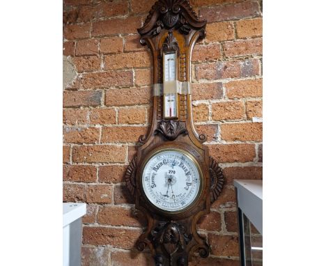A VICTORIAN CARVED OAK CASED ANEROID BAROMETER WITH AN ALCOHOL THERMOMETER ABOVE THE WHITE CERAMIC DIAL