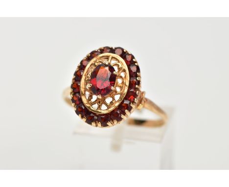 A YELLOW METAL GARNET CLUSTER RING, of an oval form, centring on a six claw set, oval cut garnet, within an open work surroun