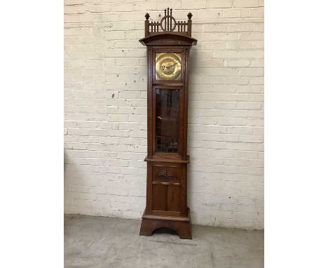 An Arts &amp; Crafts oak longcase clock with carved finials above brass face set with Arabic numerals above rectangular glaze