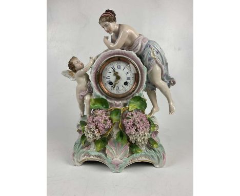 A late 19th century German porcelain figural mantel clock representing a maiden leaning towards a cherub over the arched shap