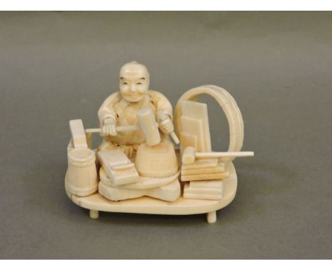 A sectional ivory carpenter, circa 1900, seated with chisel and mallet surrounded by tools and a portion of barrel, 7cm