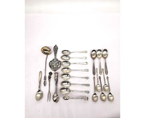 A collection of silver teaspoons, two pairs of sugar tongs, a pickle fork, a small sauce ladle and a tea strainer with bird a