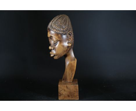 Carved Wooden Bust Signed "NGWILU"This intricately carved wooden bust depicts a stylised human head mounted on a square woode