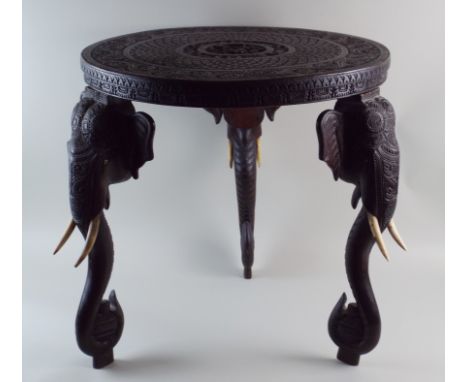 A late 19th century hardwood Indian elephant trunk table with carved circular top on three elephant head and trunk supports, 