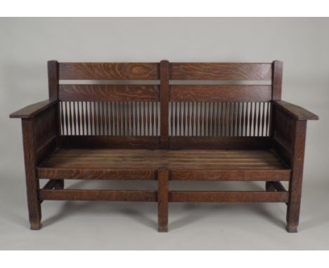 An oak Arts and Crafts settle, the double bar back over two panels of slender spindles flanked by tapering shelf arms on spin