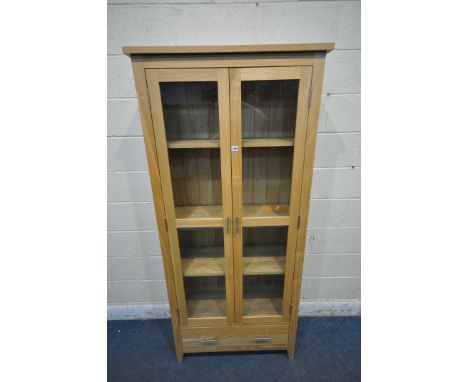 A MODERN LIGHT OAK BOOKCASE, the double glazed doors enclosing three adjustable shelves, above a single drawer, width 87cm x 