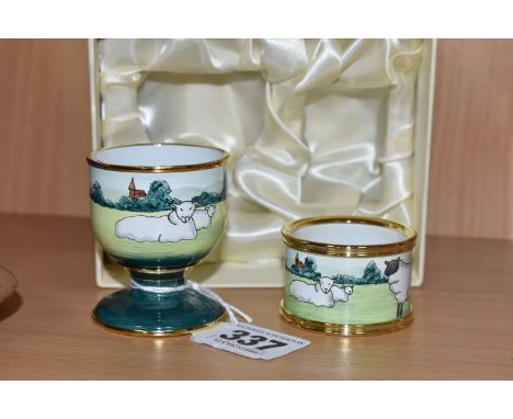 A BOXED MOORCROFT SHEEP DESIGN ENAMEL TWO PIECE BREAKFAST SET, comprising an egg cup and napkin ring, with gilt trim, printed