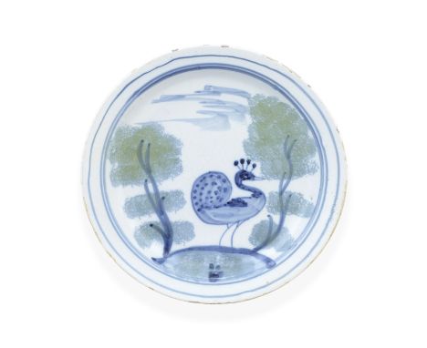 A rare London delftware 'Farmyard' plate, circa 1720-30Painted in blue with a peacock standing proud on a grassy mound betwee