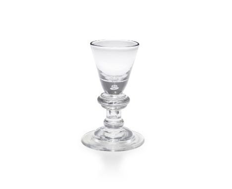 A fine heavy baluster dram glass, circa 1715The round funnel bowl with a solid base enclosing a tear, above a large triple-an