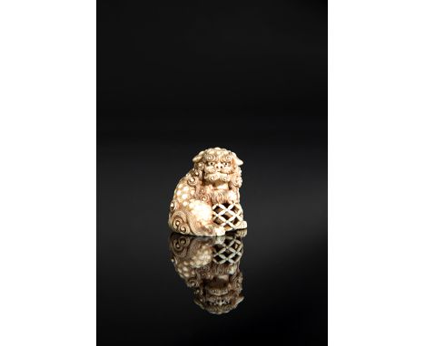 A JAPANESE IVORY NETSUKE MEIJI 1868-1912 Carved as a fierce-looking shishi, its right forepaw resting on a reticulated brocad