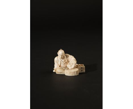 A JAPANESE IVORY OKIMONO MEIJI 1868-1912 Depicting a sculptor examining a demon mask, a small cabinet and tools by his side, 