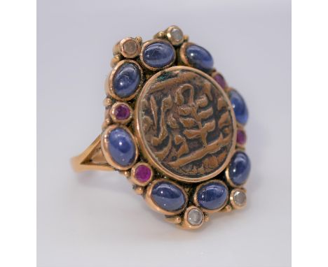 A yellow metal (tested as gold) Islamic coin, sapphire, ruby and diamond dress ring. Set to the centre with an Islamic coin m