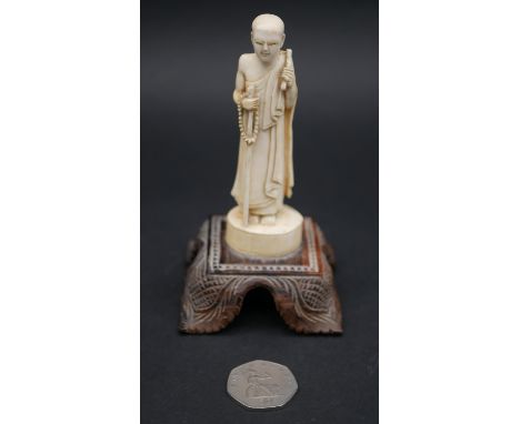 An antique carved Chinese ivory statue of a Luohan mounted on a floral form hardwood base. H.13cm 