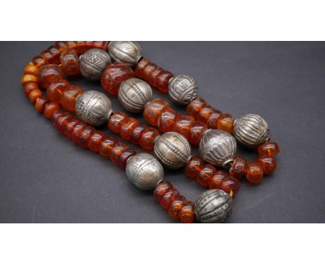 A Tibetan white metal and amber necklace. Strung with fifty seven polished amber beads, the largest measuring 2.5 cm in diame