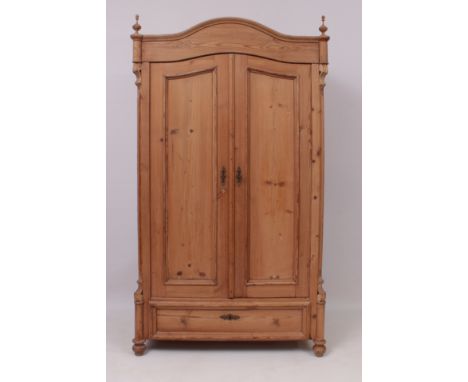 A French-style waxed pine wardrobe - the arched pediment with turned finials over two panelled doors and a single long drawer