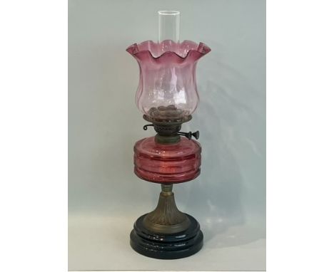 An early 20th century brass and cranberry glass oil lamp - with faceted cranberry glass reservoir and clear to cranberry glas